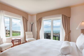 A hotel room with a large bed, a chair, a small table, and a view of the ocean. - Praia D'El Rey Marriott Golf & Beach Resort (Obidos)