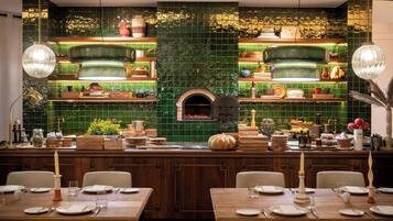A restaurant with a green-tiled backsplash, wooden tables, and a central island with a built-in oven.