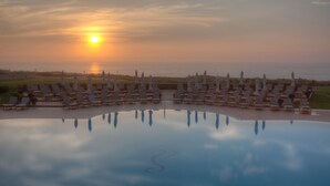 A poolside area with lounge chairs and umbrellas, reflecting the sunset over the water. - Praia D'El Rey Marriott Golf & Beach Resort (Obidos)