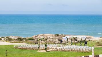 Montaje para una ceremonia de boda con filas de sillas y un altavoz, con vista a una playa y al océano.