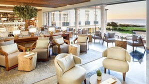 A spacious lounge area with multiple seating options, a large tree, and a view of the sea. - Praia D'El Rey Marriott Golf & Beach Resort (Obidos)
