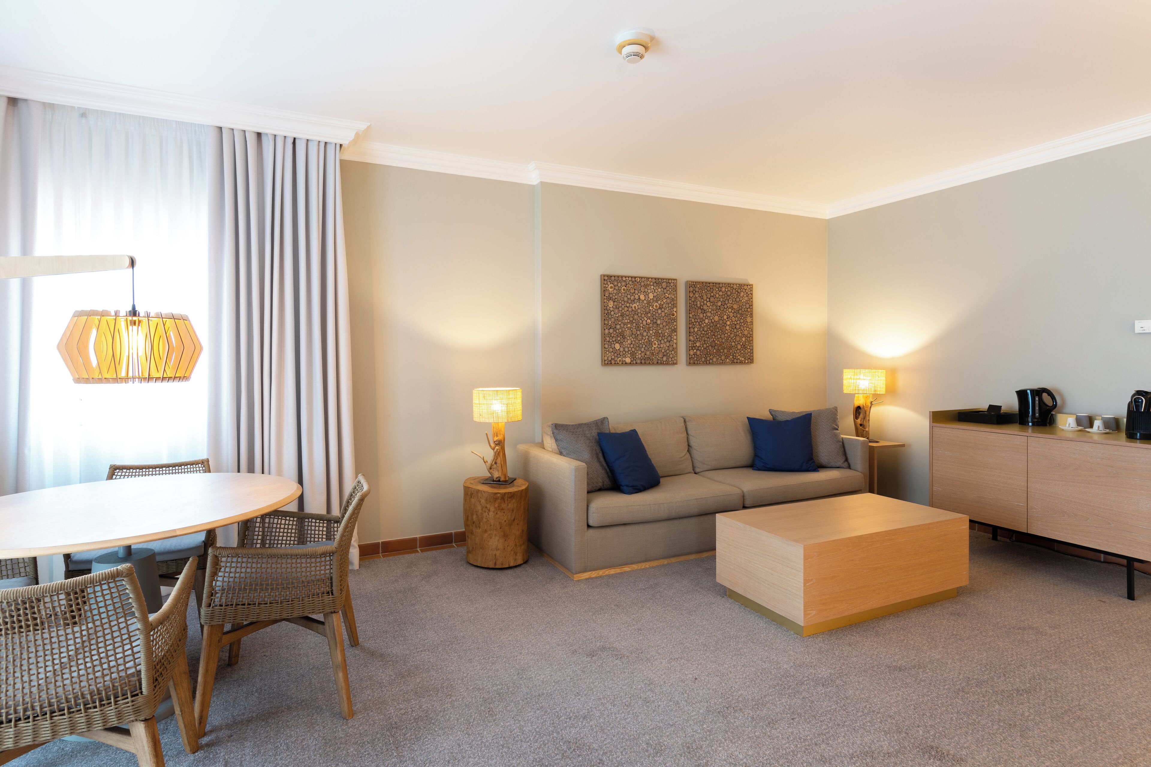 Ein modernes Wohnzimmer mit rundem Tisch, Korbstühlen, einer Couch, einem Couchtisch und zwei Lampen.