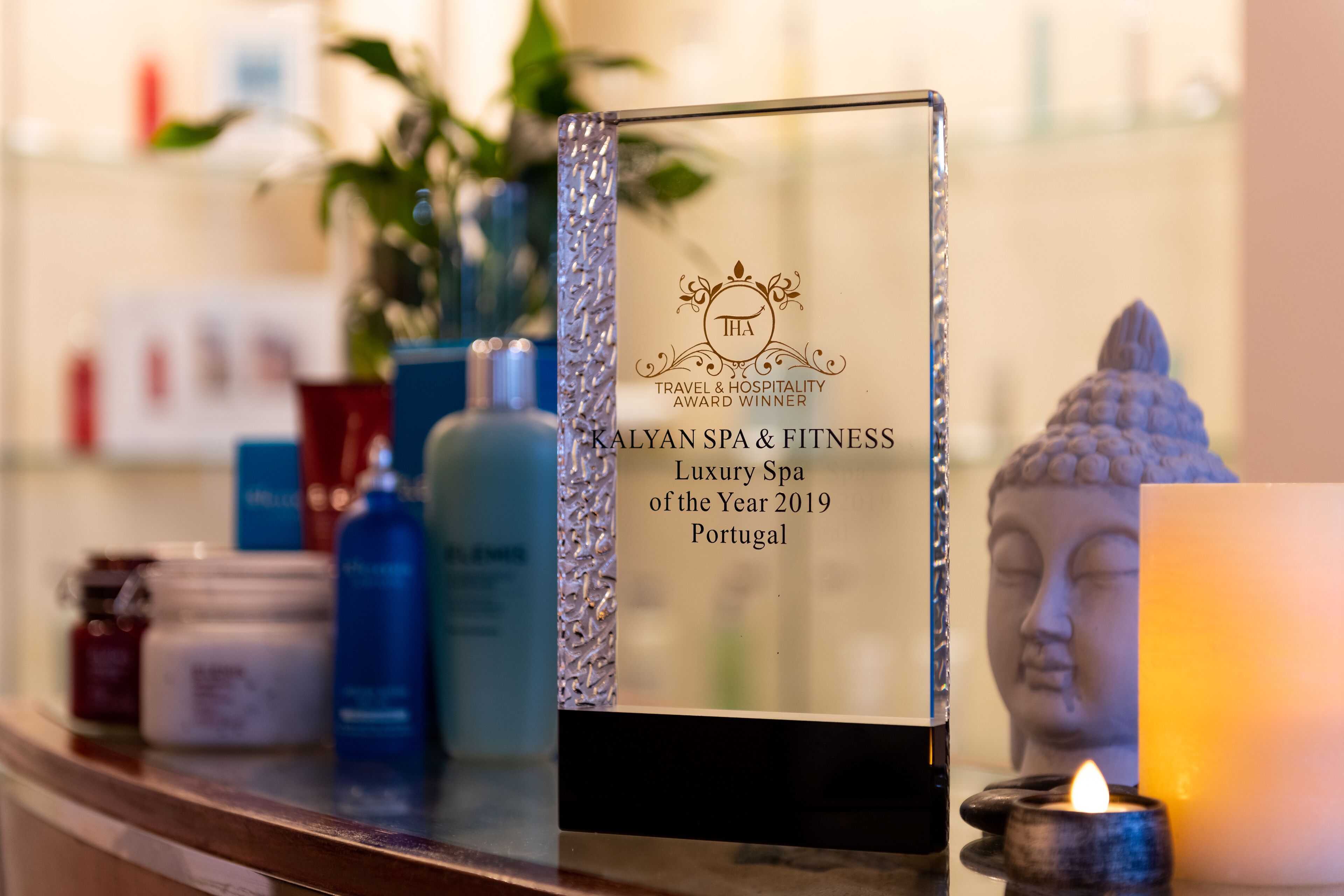 A plaque on a counter with the text "KALYAN SPA & FITNESS Luxury Spa of the Year 2019 Portugal" and a Buddha statue in the background.