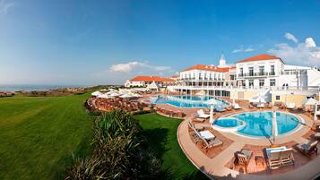 Un gran complejo turístico con piscina central, varias zonas de descanso y vistas al océano.