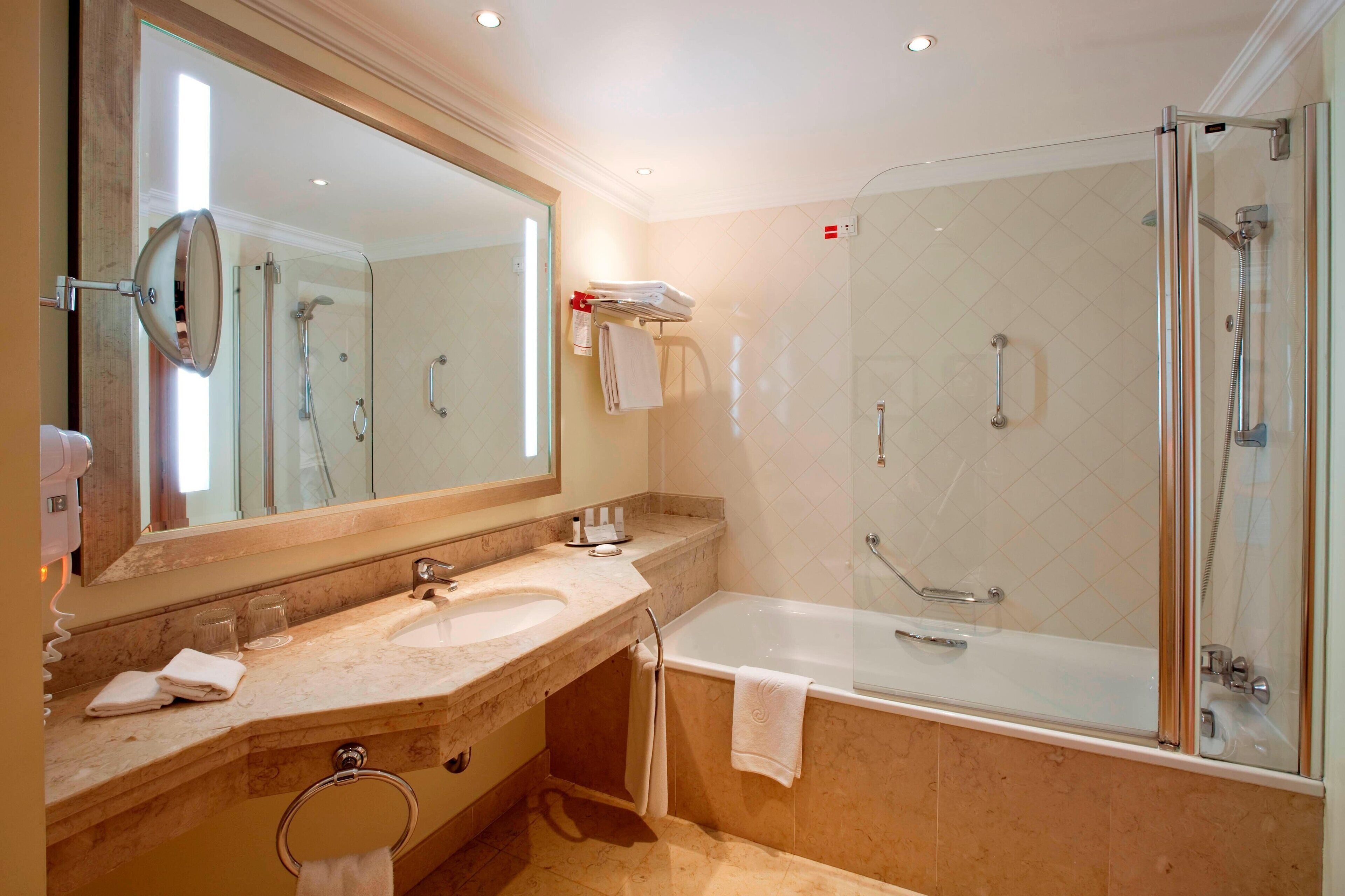 A modern bathroom with a glass-enclosed shower, a large mirror, and a marble sink.