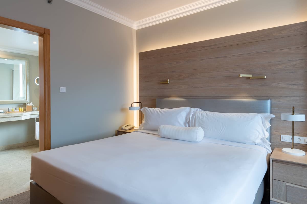A neatly made bed with white linens, a wooden headboard, bedside lamps, and a nightstand with a phone and a lamp.