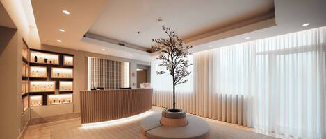 Un hall d’entrée moderne avec un comptoir d’accueil, un bac à fleurs en bois contenant un arbre et un sol recouvert de moquette.