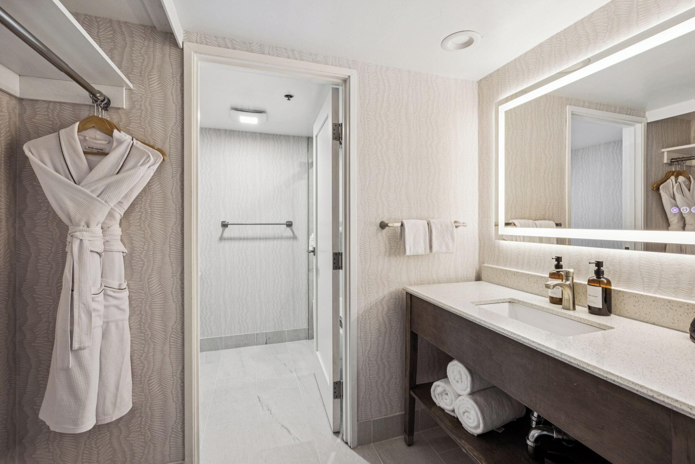 A modern bathroom with a large mirror, a white sink, and a robe hanging on a rack.