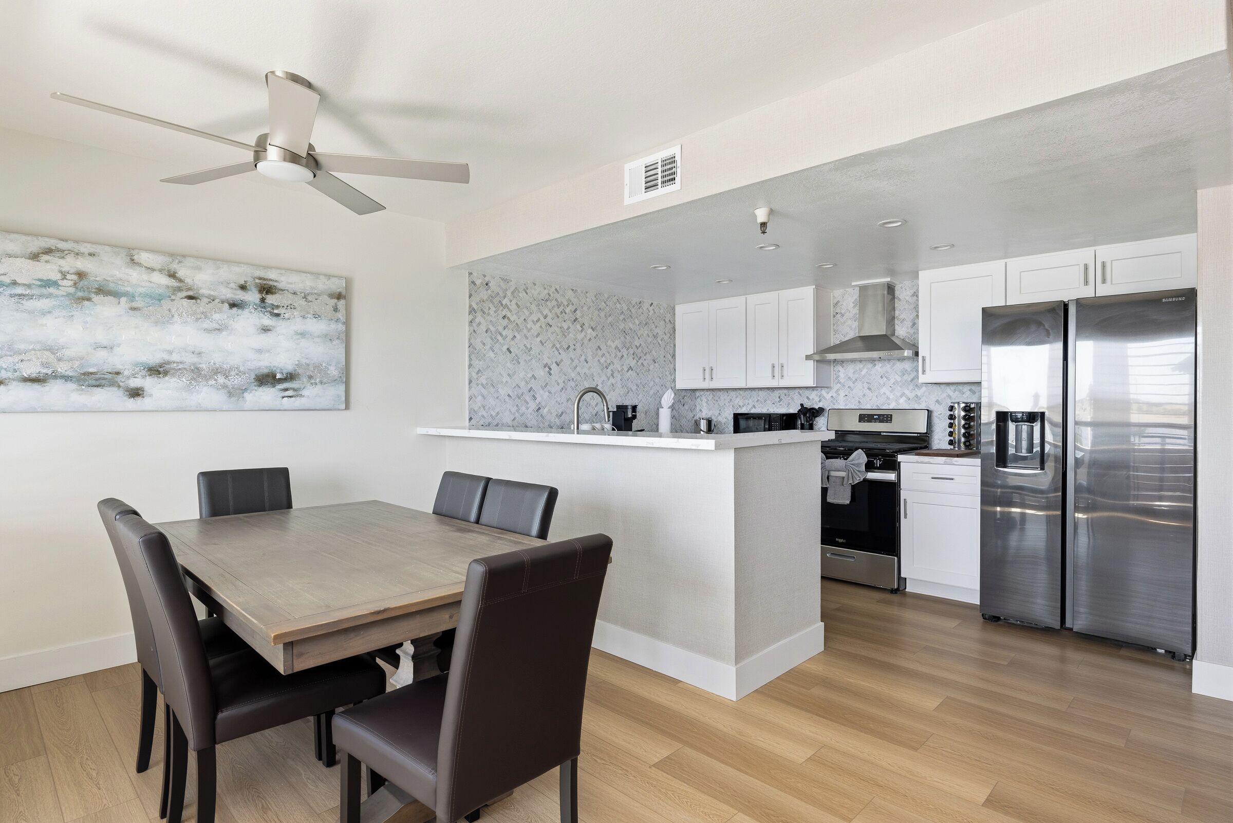 A modern kitchen with a central island, stainless steel appliances, and a dining area with a wooden table and chairs.