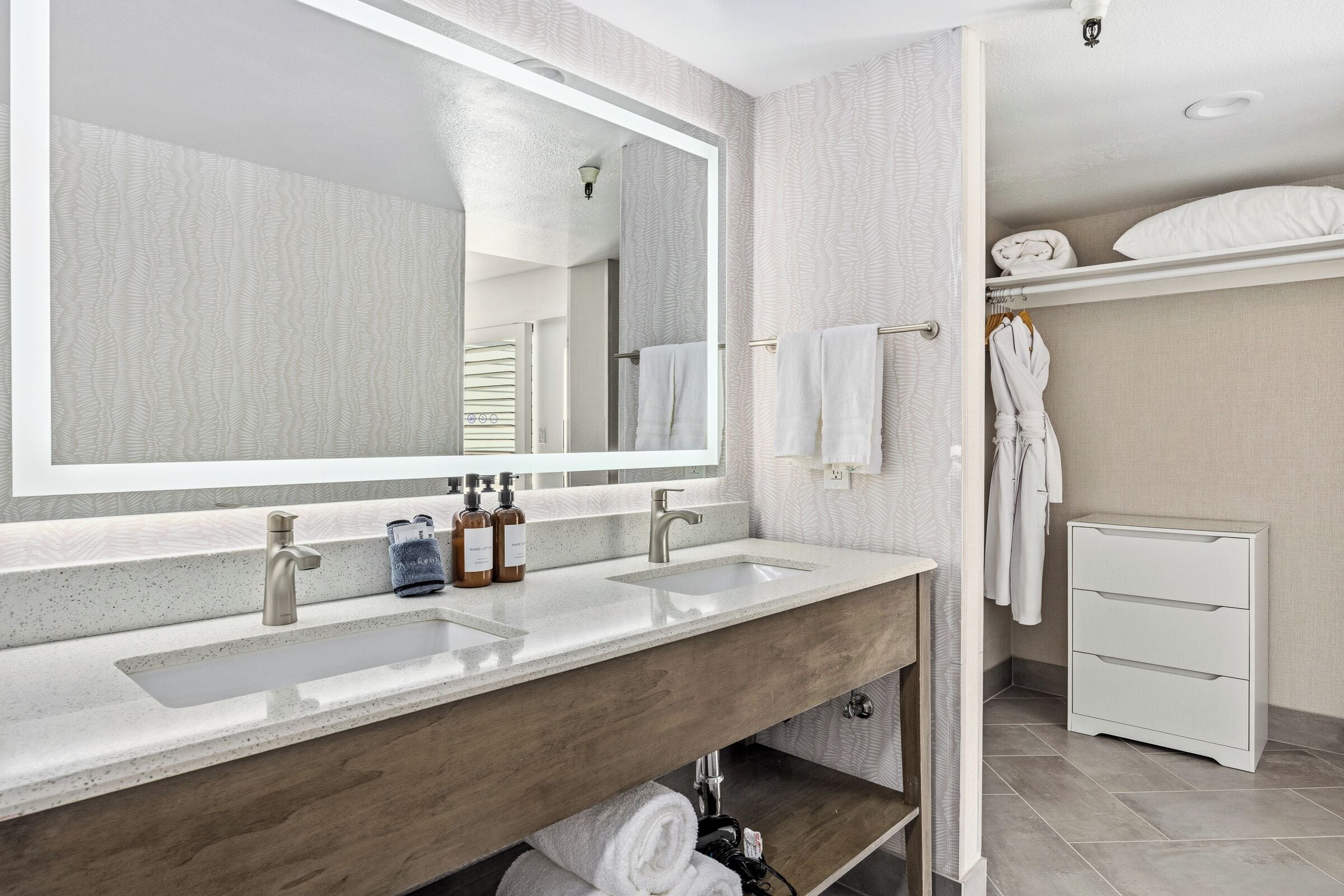 Un baño moderno con un espejo grande, dos lavamanos, un mueble de tocador de madera, un perchero y un armario.