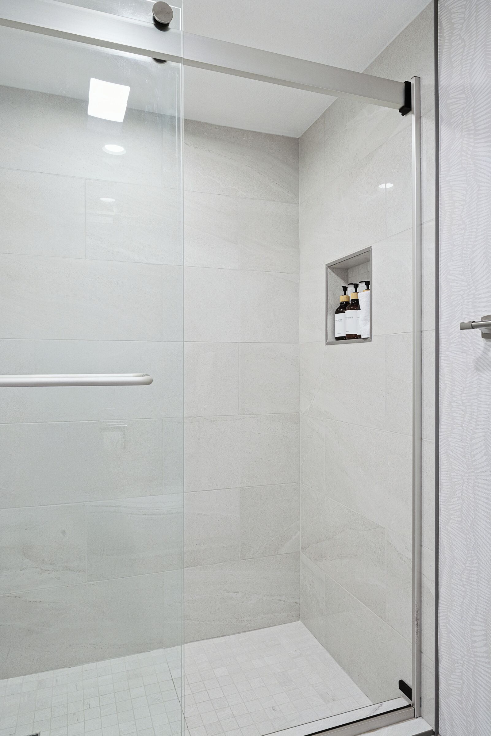 A modern shower with a glass door, a handrail, and a small shelf with toiletries.