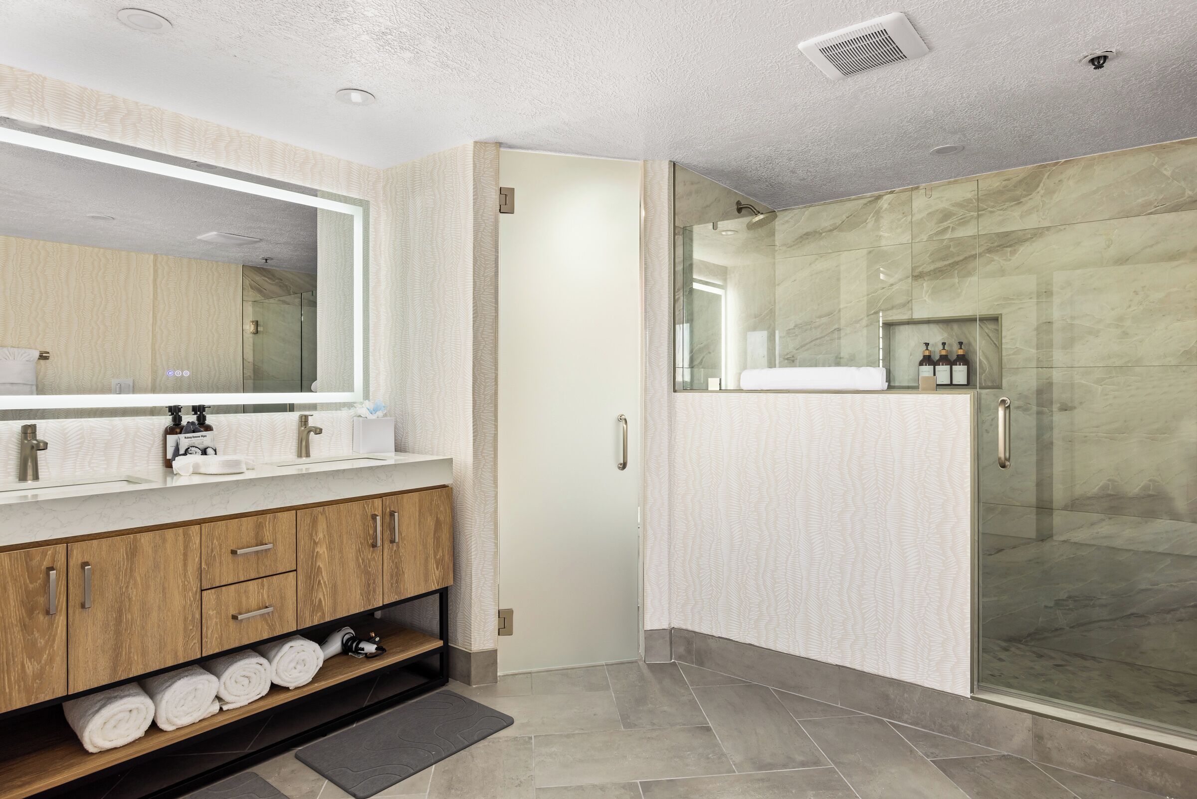 A modern bathroom with a large mirror, wooden vanity, and a glass shower enclosure.
