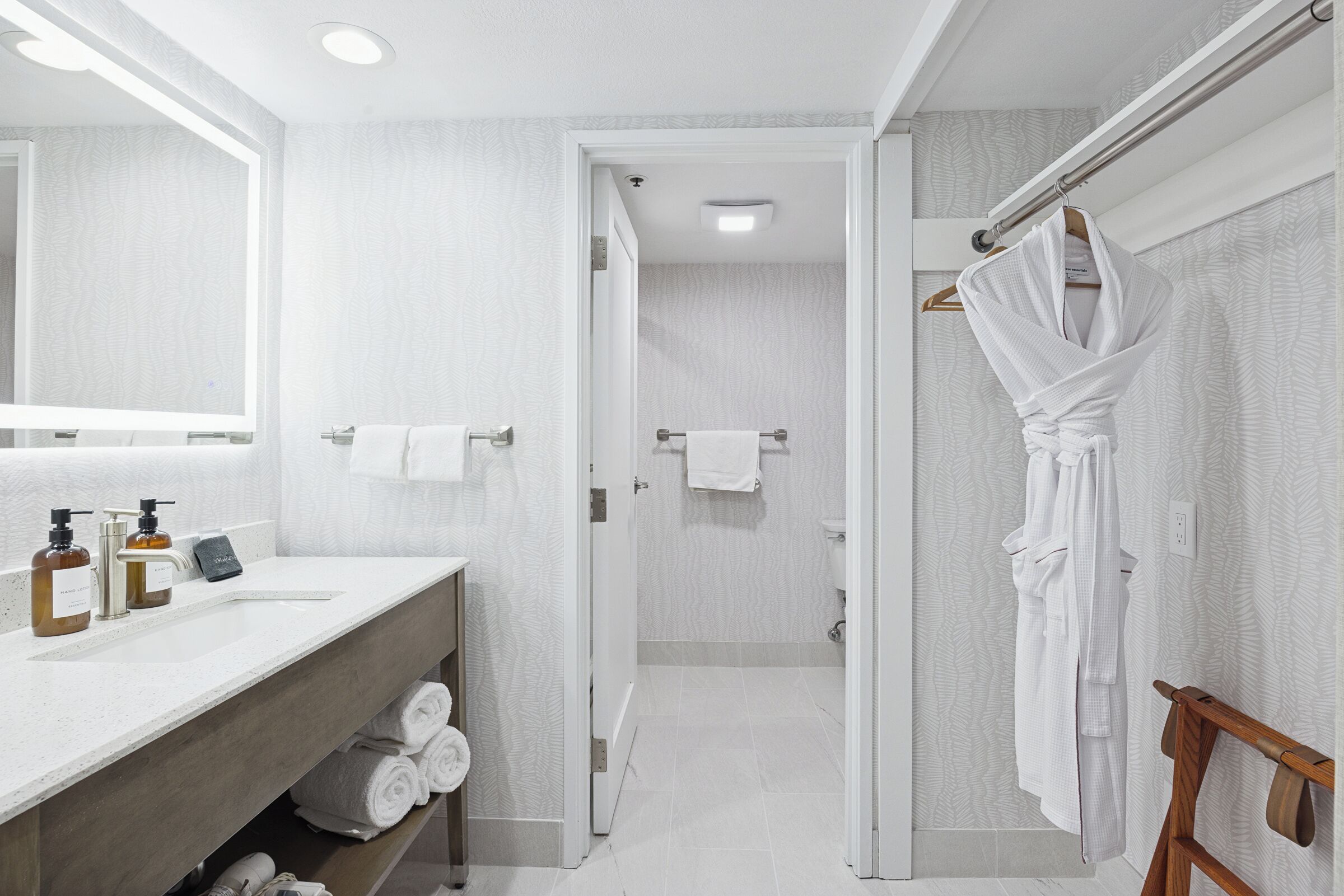 A modern bathroom with a vanity, towel rack, and a robe hanging on a wooden hanger.