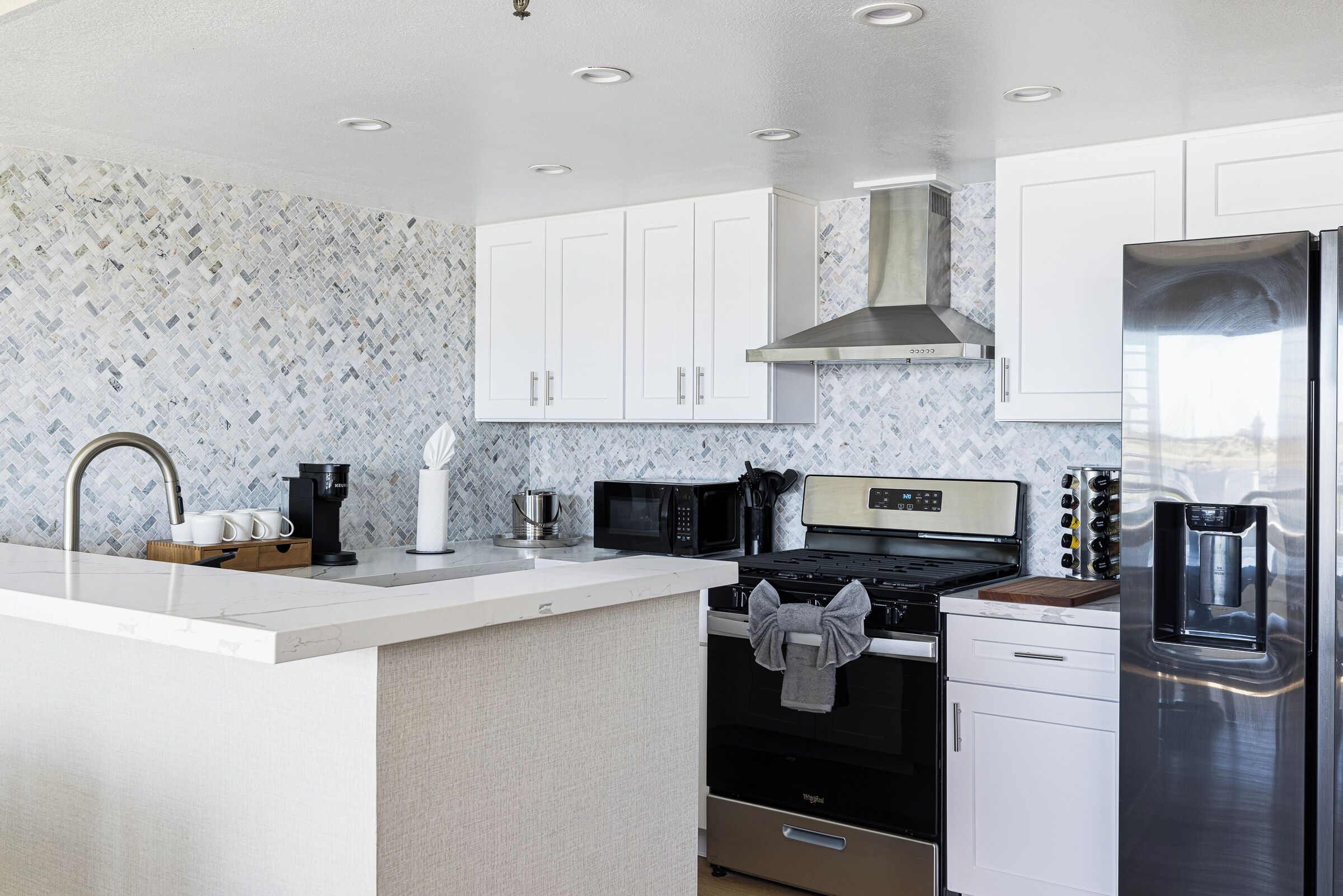 A modern kitchen with white cabinetry, a stainless steel refrigerator, a microwave, a stove, and a coffee maker.