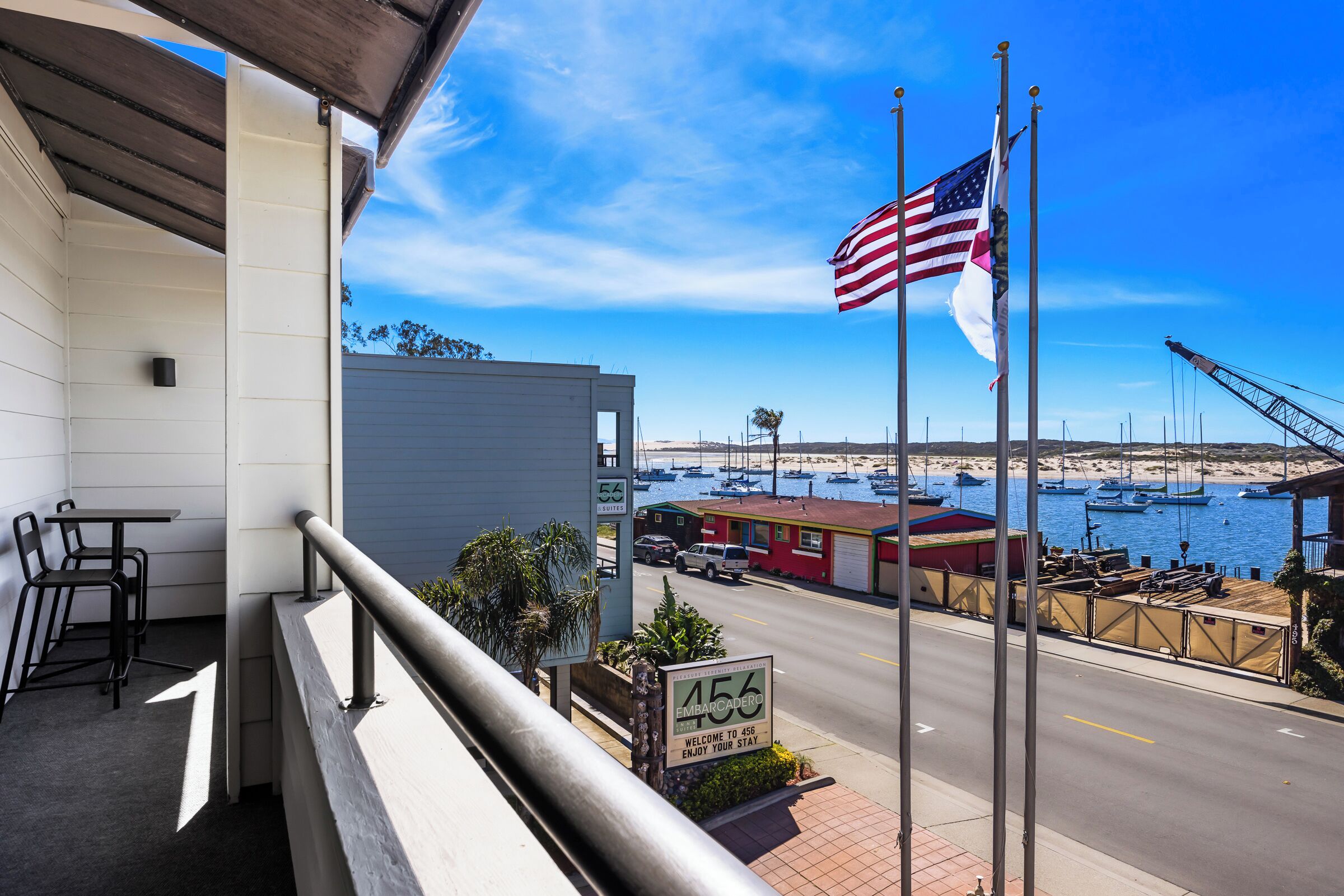 A balcony with a view of the marina, a sign for '456 Embarcadero,' and an American flag.