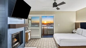 A hotel room with a fireplace, a bed, a desk, and a balcony with a sunset view. - 456 Embarcadero Inn & Suites (Morro Bay)