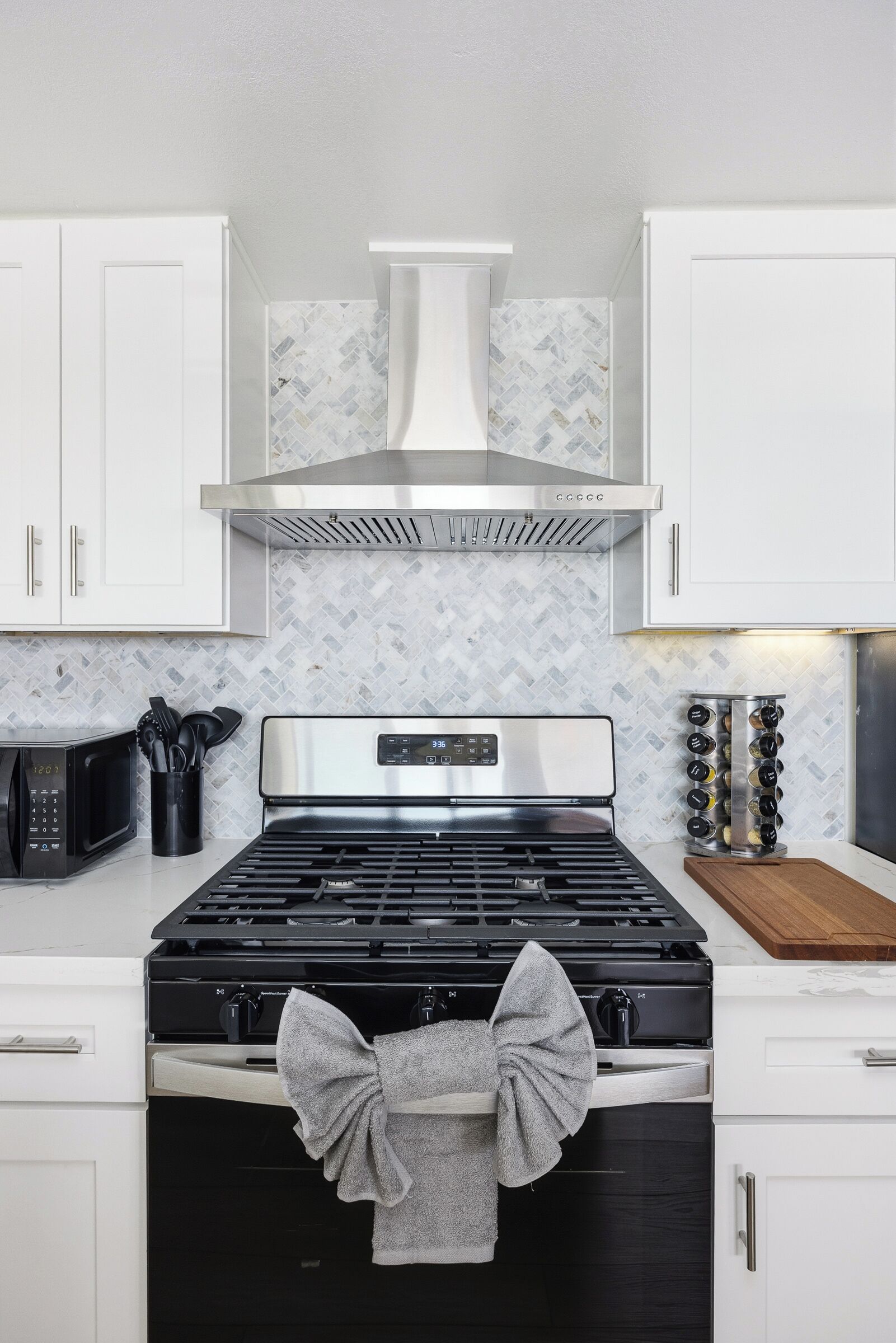 Uma cozinha com armários brancos, fogão de aço inoxidável, micro-ondas e painel de azulejos.