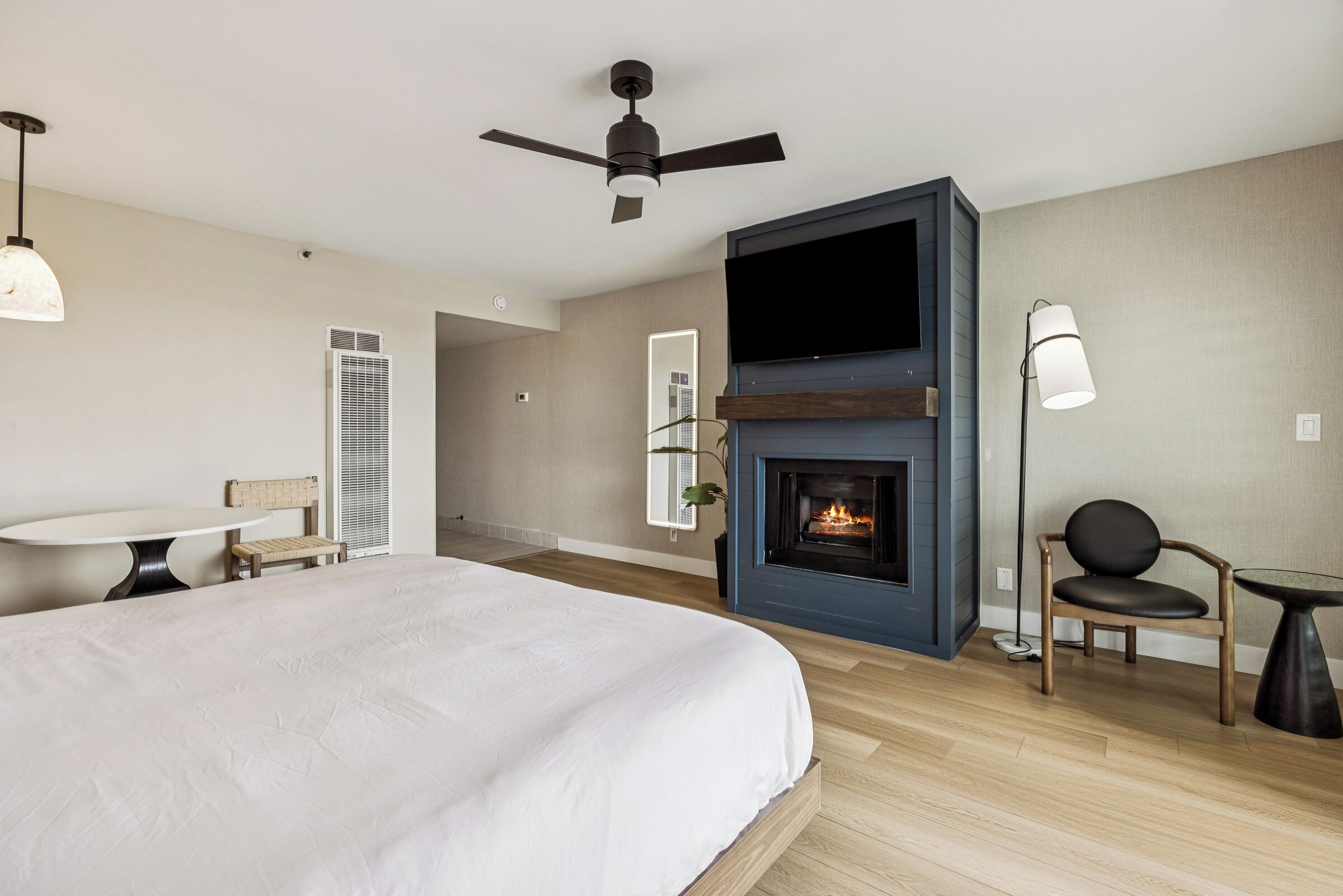 A bedroom with a bed, a fireplace, a ceiling fan, a TV, and a chair.