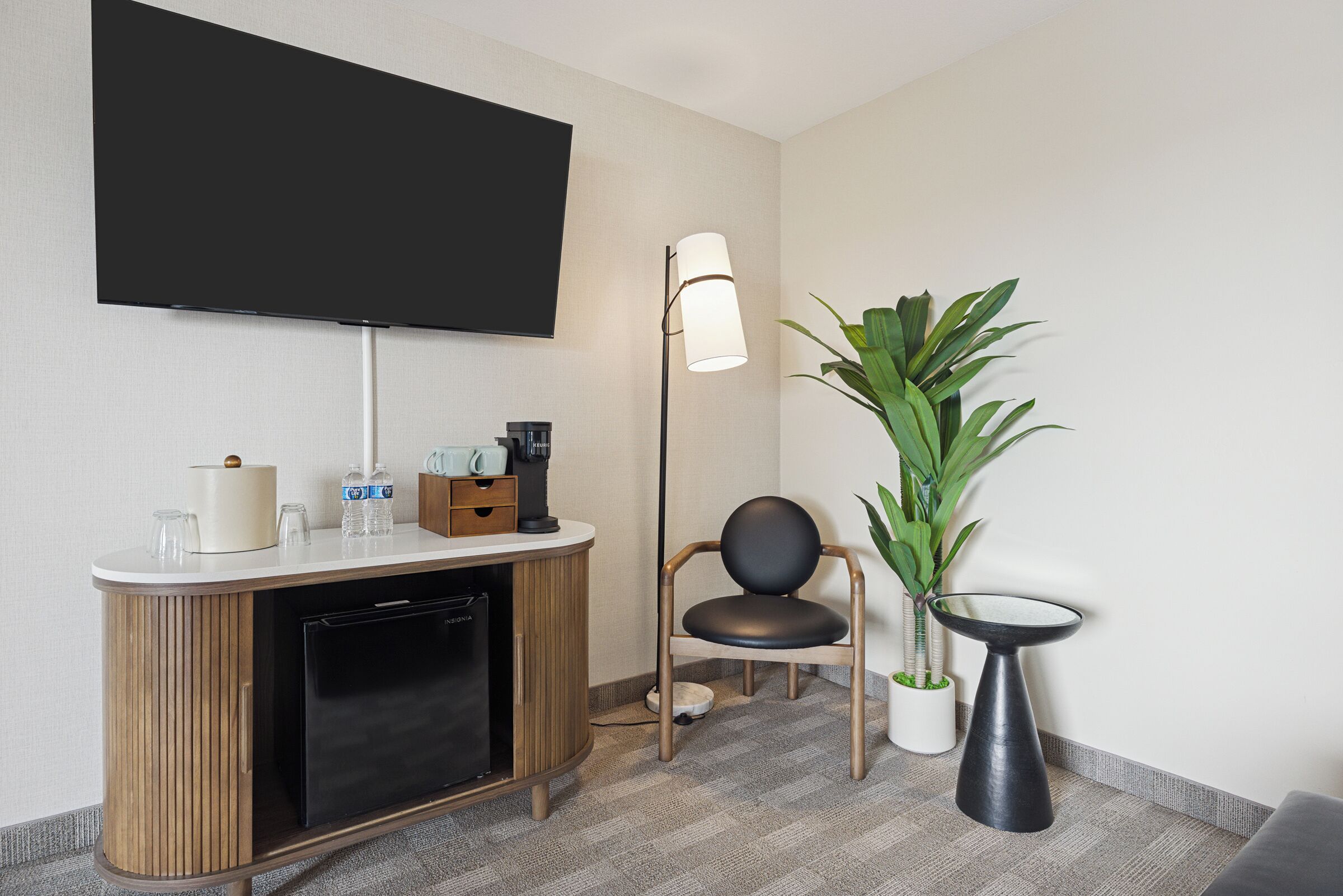 Une chambre d’hôtel équipée d’un téléviseur à écran plat, d’une armoire en bois, d’une chaise, d’une plante en pot et d’un lampadaire.