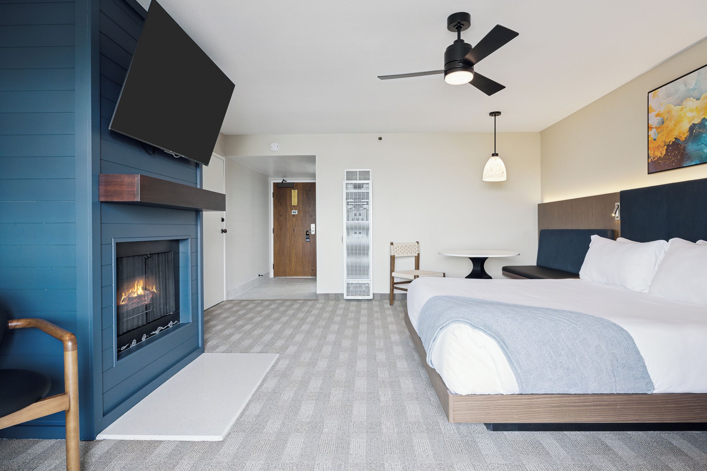 A hotel room with a fireplace, a bed, a ceiling fan, a dining table, and a chair.
