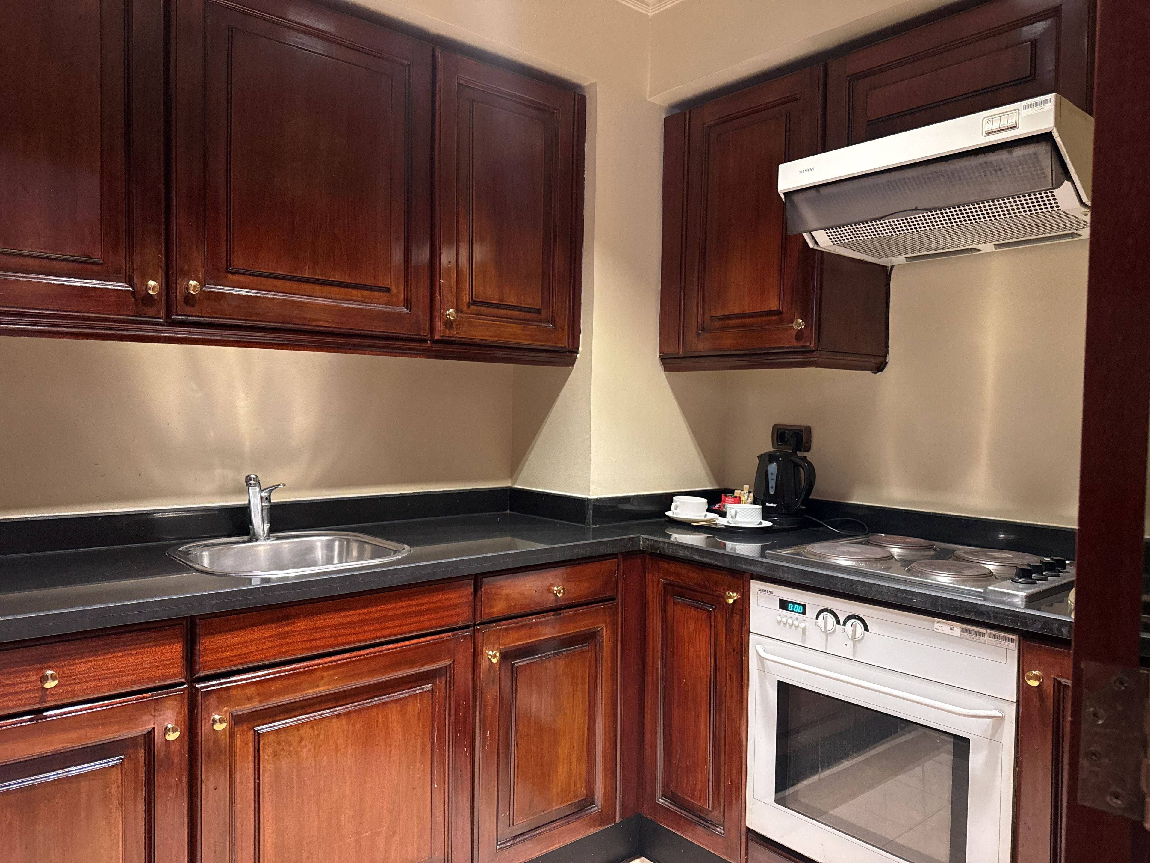 A kitchen with wooden cabinets, a stainless steel sink, a coffee maker, and a white oven.