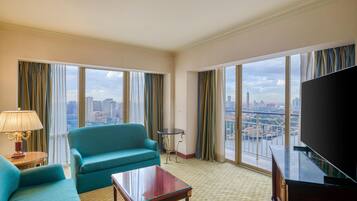 Une chambre d’hôtel avec une grande fenêtre, un canapé de couleur turquoise, une petite table ronde et un téléviseur.