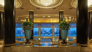Un vestíbulo con columnas de mármol, un mostrador de recepción y grandes ventanales con vista a la ciudad.
