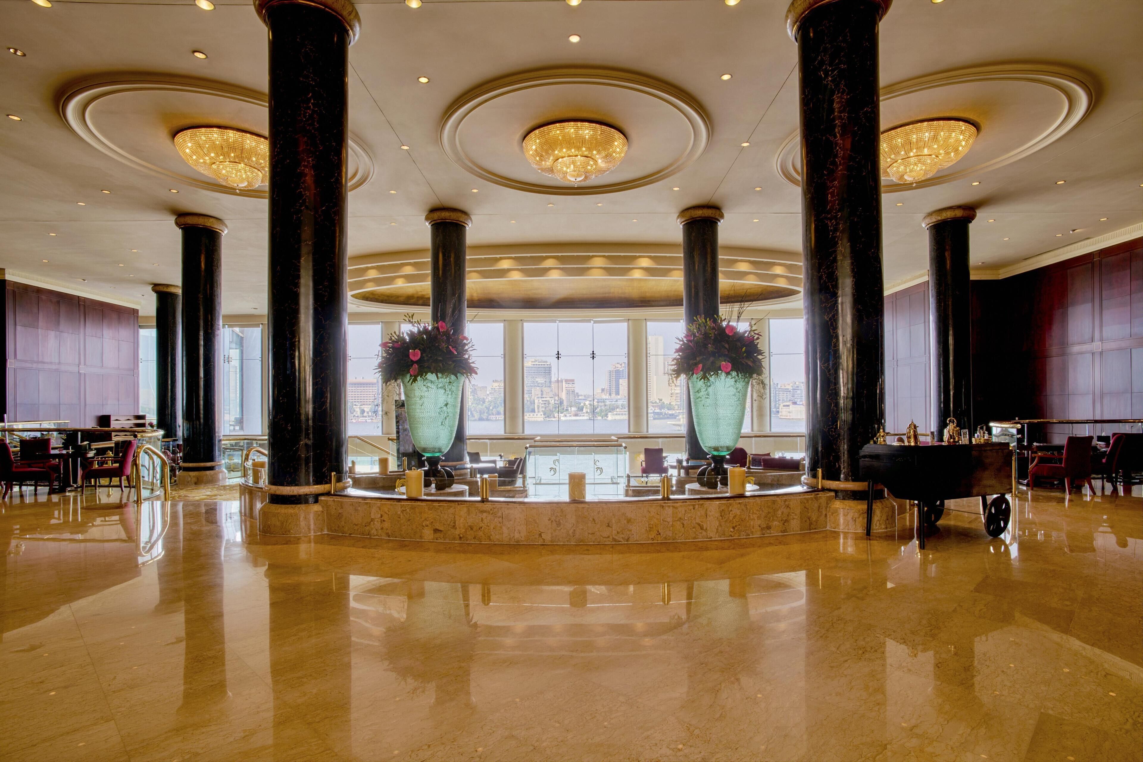 A spacious lobby with marble flooring, large columns, chandeliers, and a reception desk.