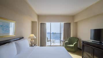 Ett hotellrum med en stor säng, en tv, en stol, ett litet bord och en balkong med utsikt.