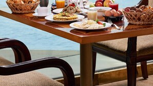 Una mesa de desayuno con comida y bebidas, con vista a una masa de agua donde se ve un velero y edificios al fondo.