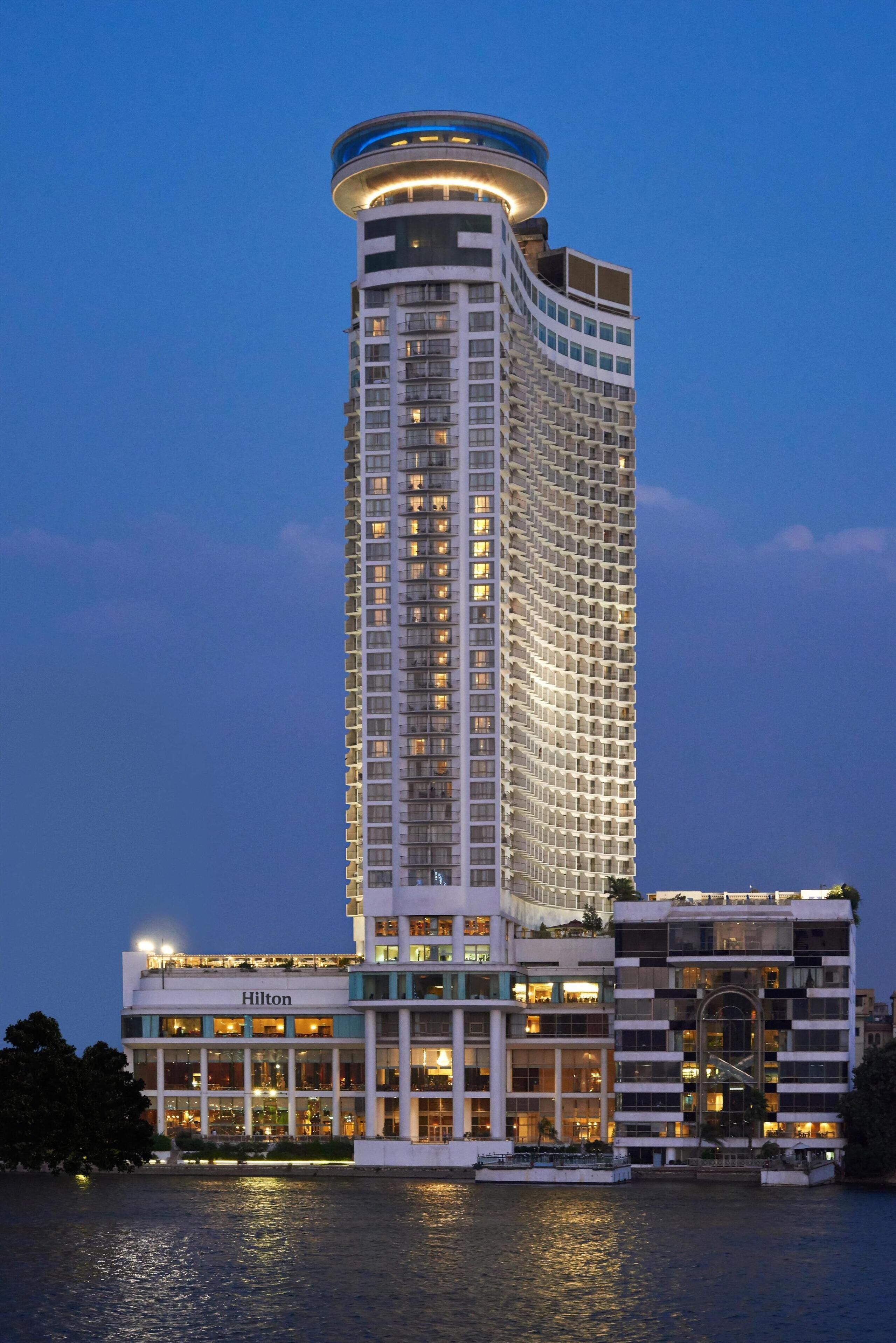A tall, modern hotel with a curved top, multiple floors, and a waterfront location.