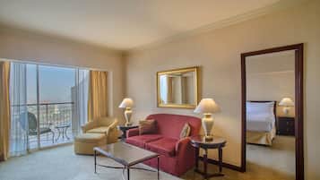 A hotel room with a red sofa, a glass table, a chair, a bed, and a large mirror.