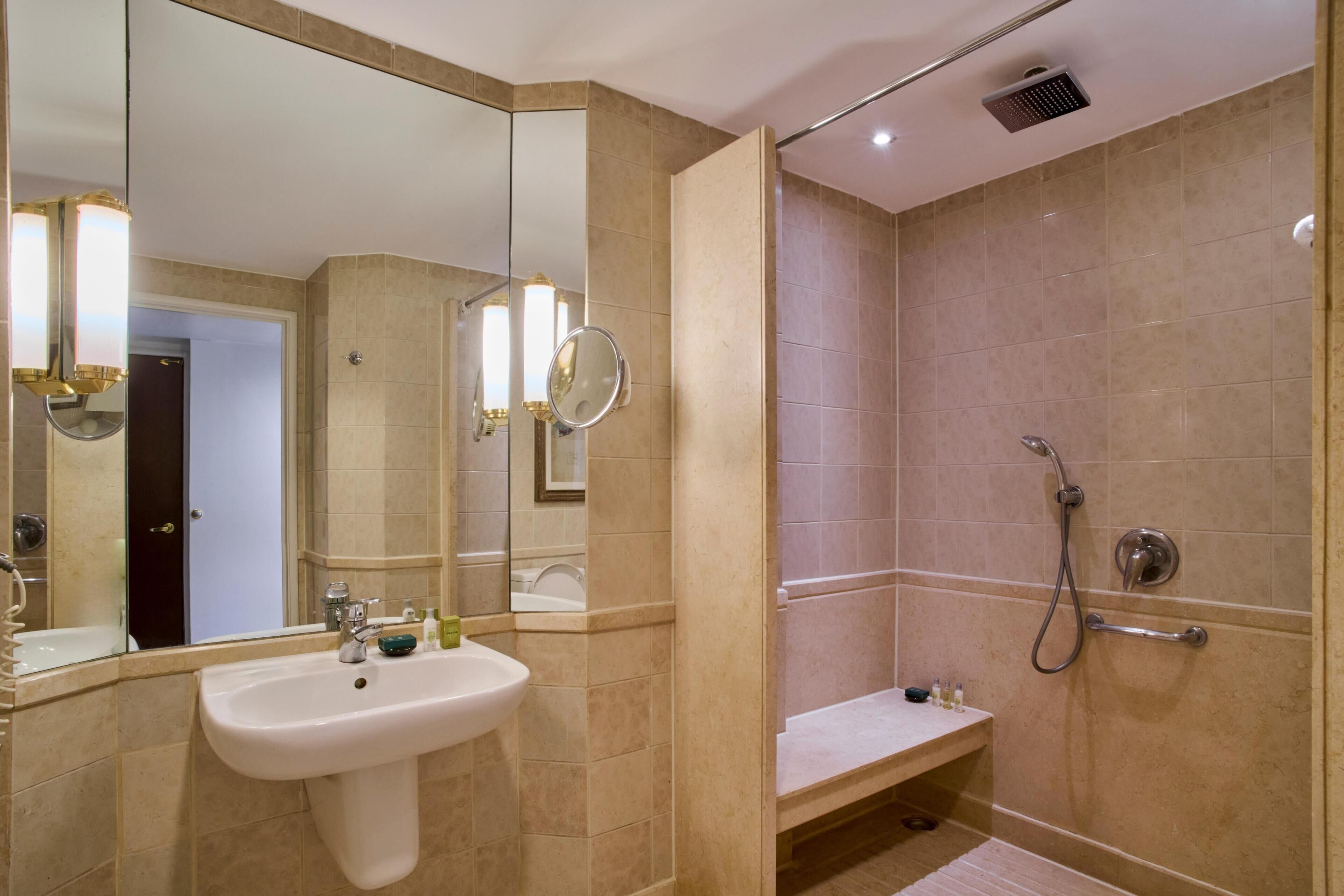 A bathroom with a sink, mirror, shower, and a bench.