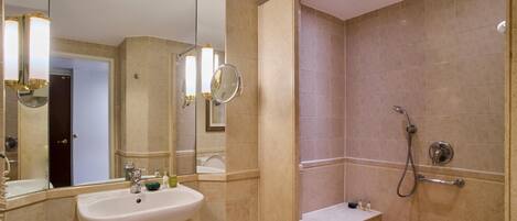 A bathroom with a sink, mirror, shower, and a bench.