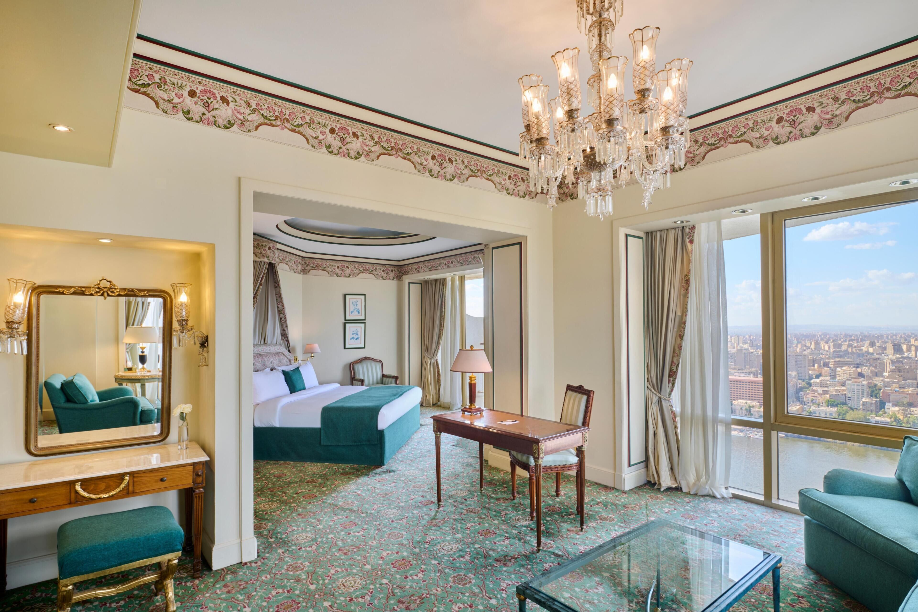 Une chambre d’hôtel avec un grand lit, un coin salon avec une table et des chaises, un miroir et une vue sur la ville.