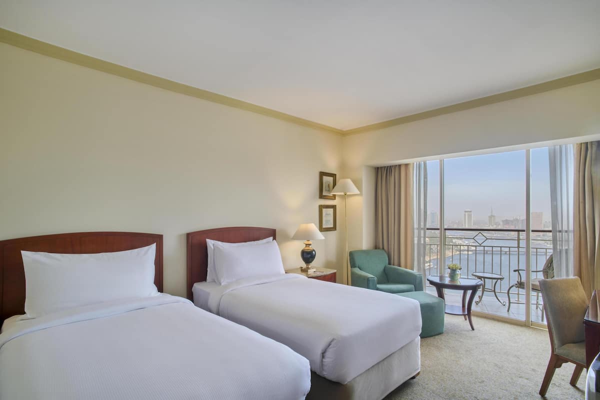 A hotel room with two beds, a balcony with a view, a small table, and a chair.