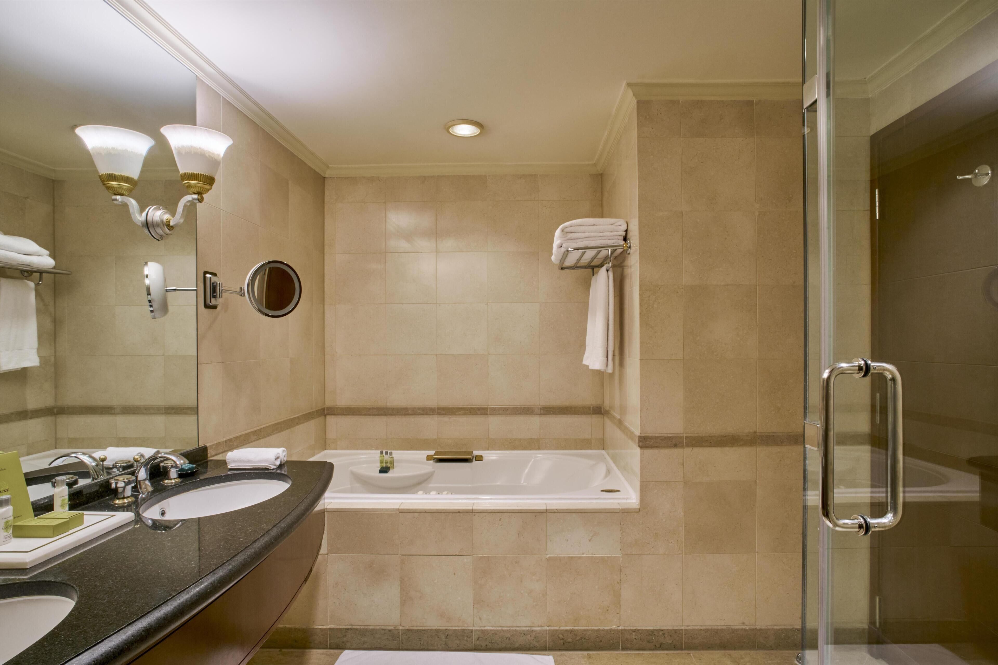 A modern bathroom with two sinks, a bathtub, a glass shower enclosure, and a vanity mirror.