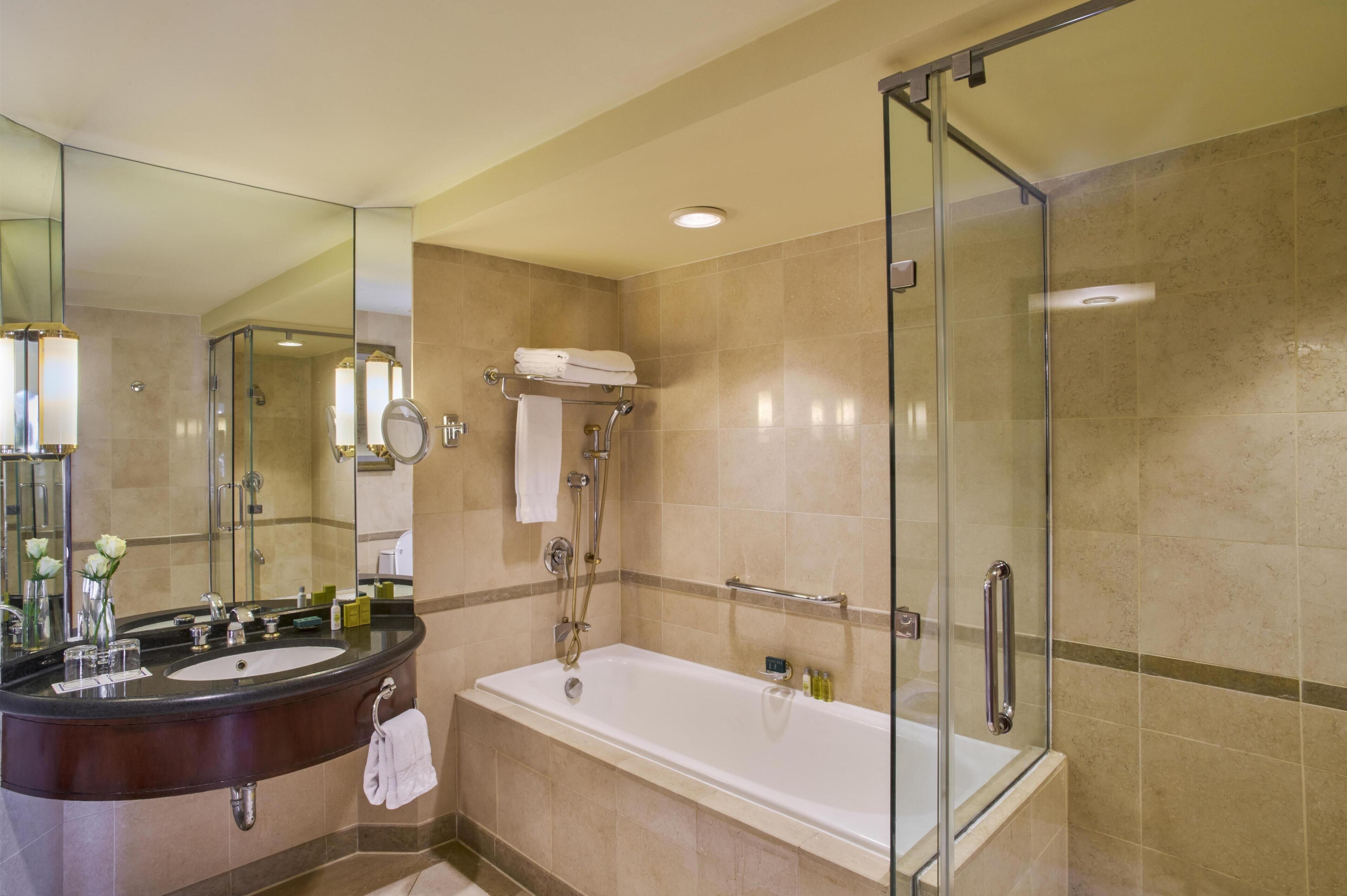 A modern bathroom with a glass-enclosed shower, a large bathtub, a vanity with a mirror, and a towel rack.