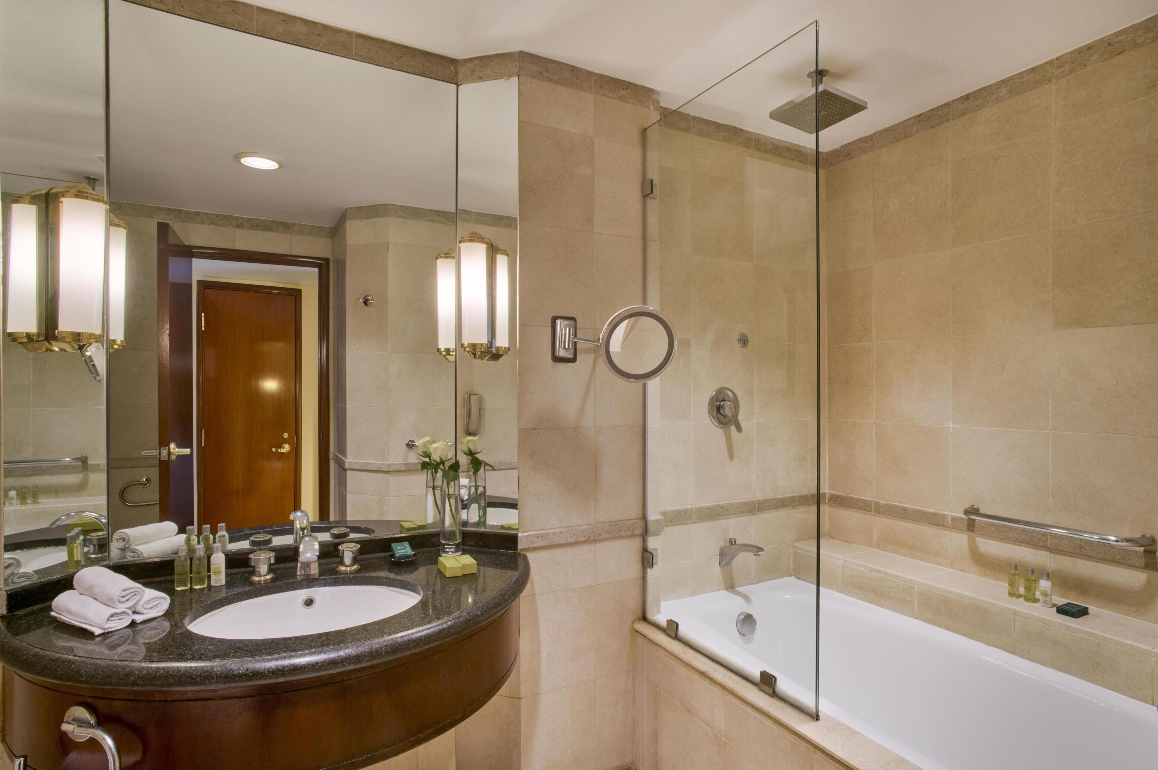 A bathroom with a large mirror, a sink, a bathtub, and a shower.