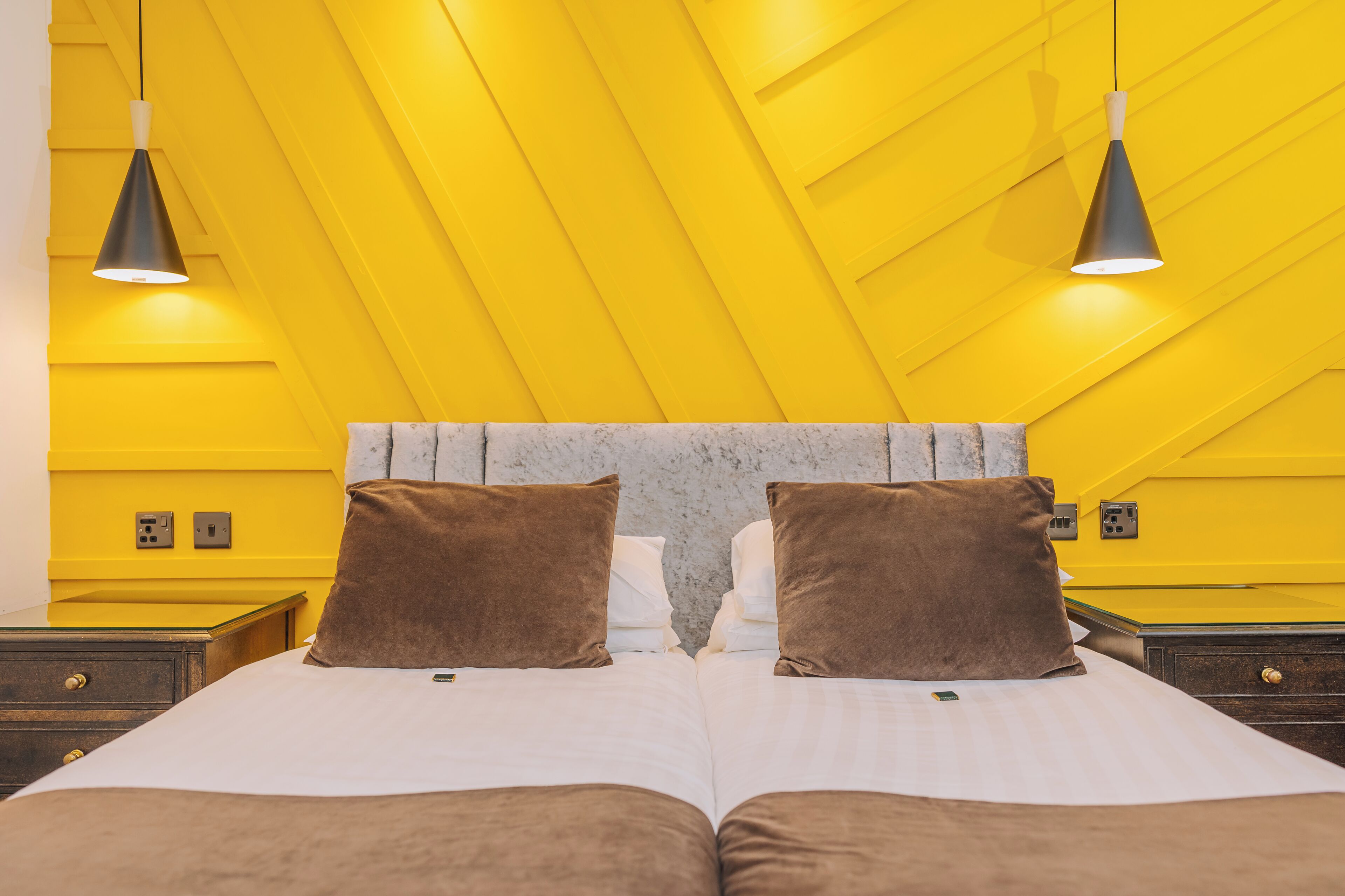 A room with a bed, two bedside tables, and two pendant lights.