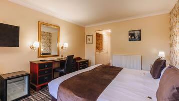 A hotel room with a bed, a desk, a chair, a dresser, a small refrigerator, and a mirror.