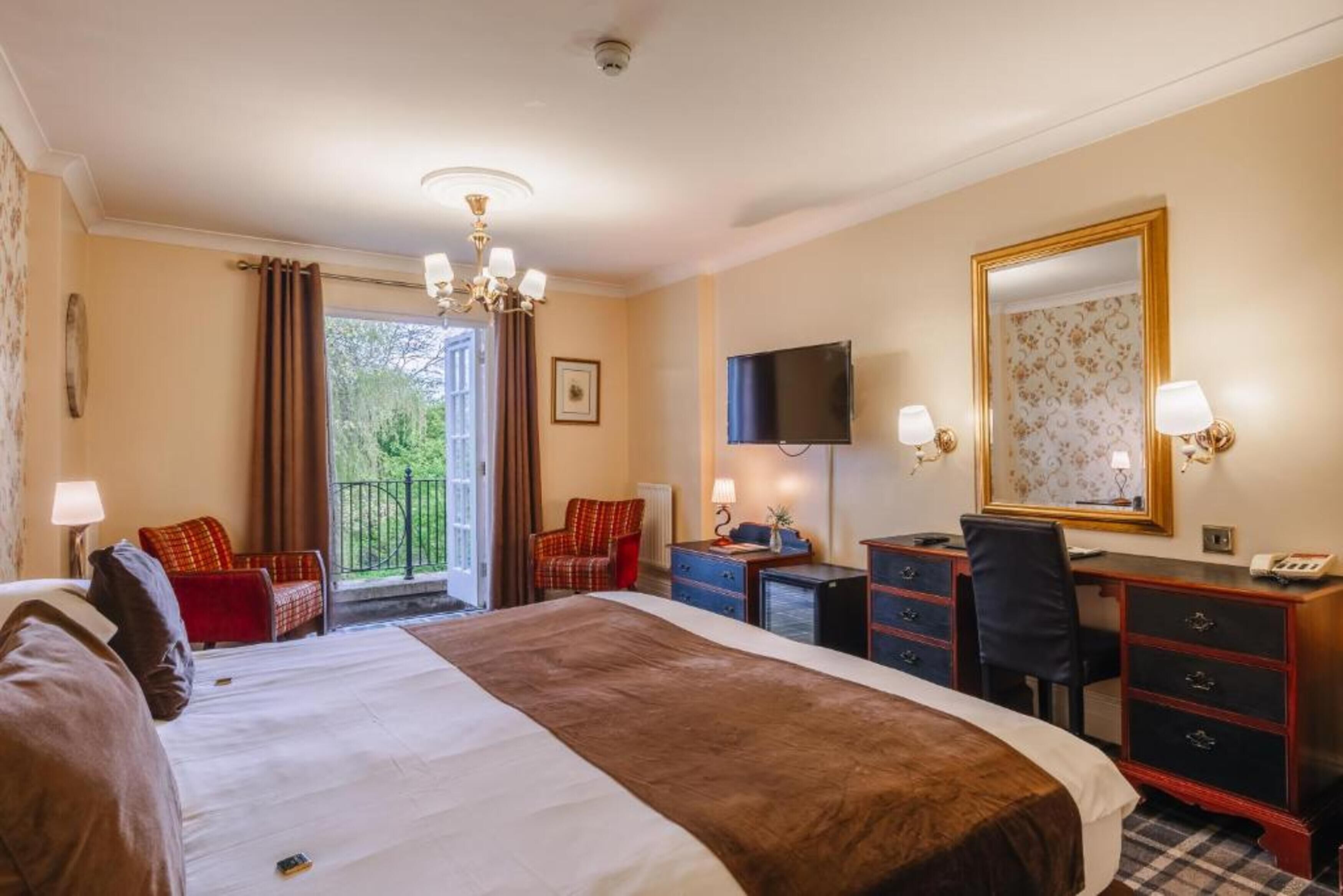 A hotel room with a large bed, a desk, a chair, a television, and a balcony with curtains.