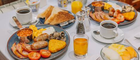 Una mesa de desayuno con platos de huevos, tocino, salchichas, tostadas y fruta. También hay tazas de café y jugo.