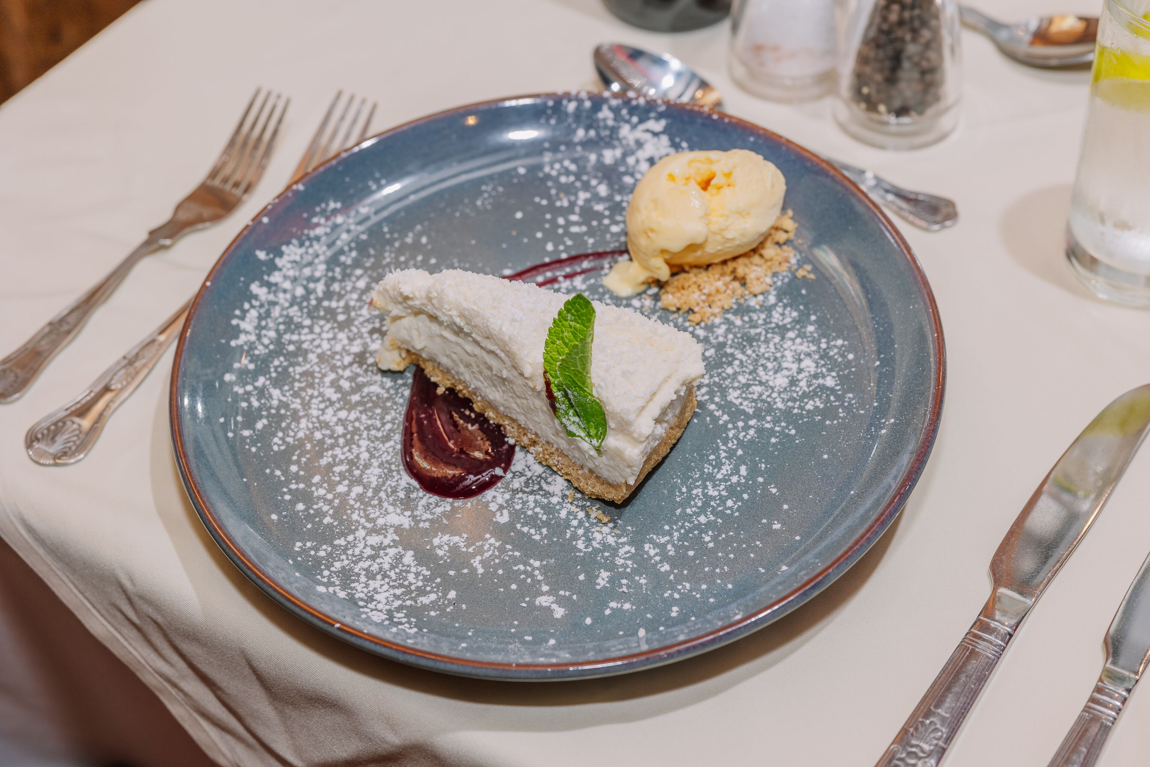A dessert plate with a slice of cake, a scoop of ice cream, and a mint leaf on a blue plate.
