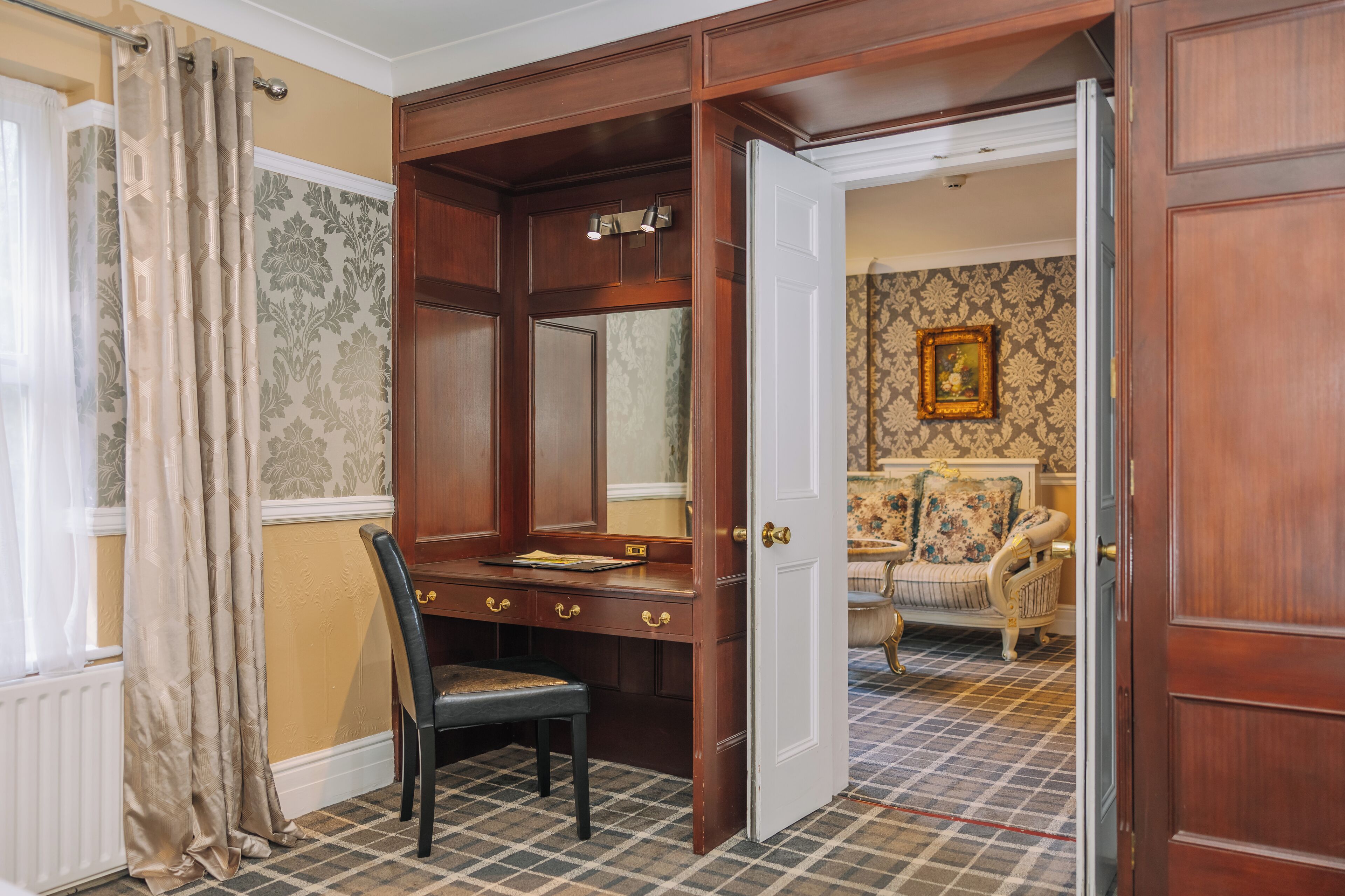 A room with a wooden desk, a chair, a door, and a patterned carpet.