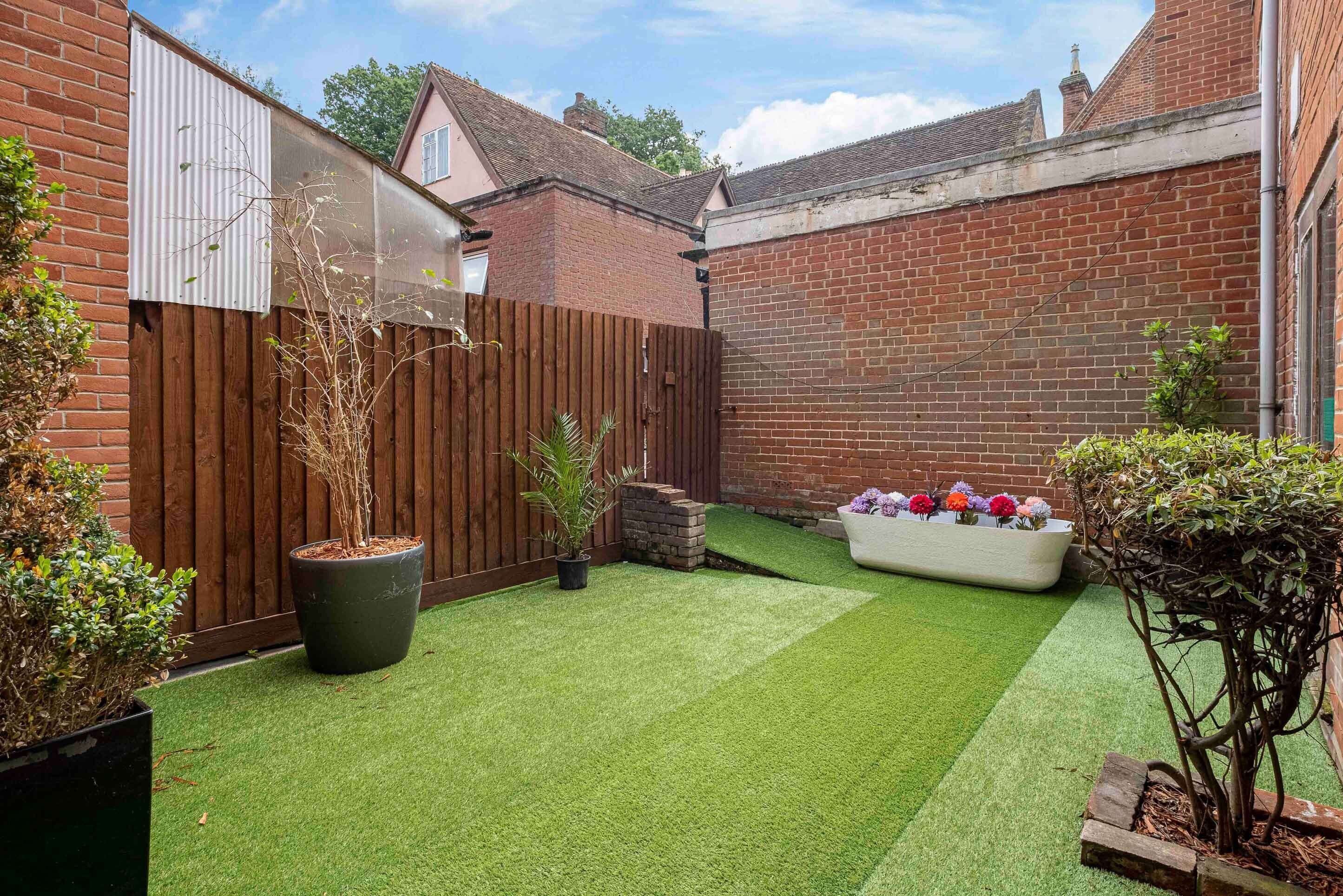 A backyard with artificial grass, a wooden fence, and a brick wall.