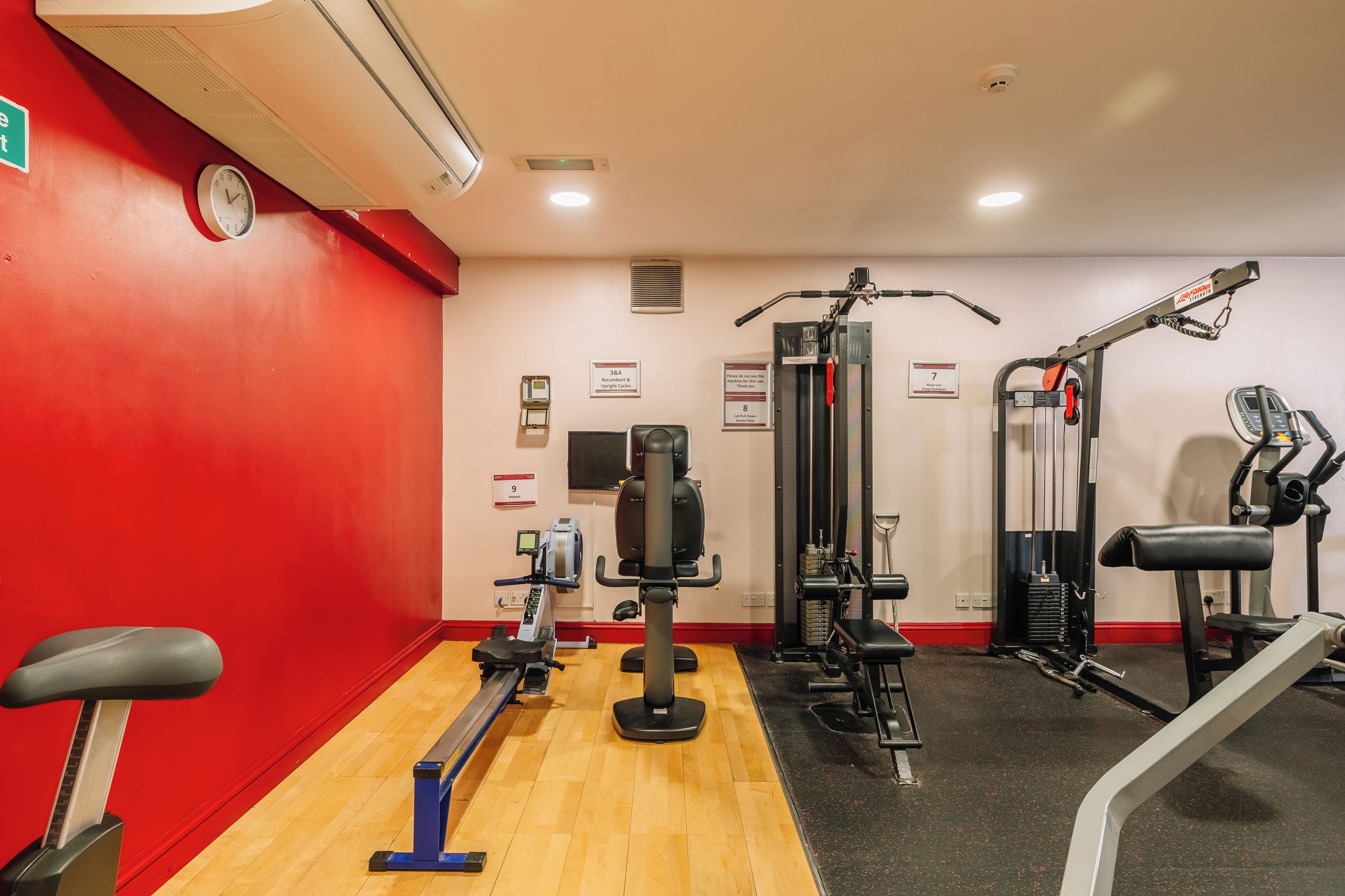 A gym with cardio equipment, weight machines, and a red wall.