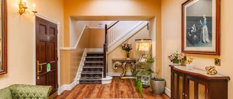 A hallway with a staircase, a green sofa, a patterned rug, a wooden cabinet, and a framed picture on the wall.