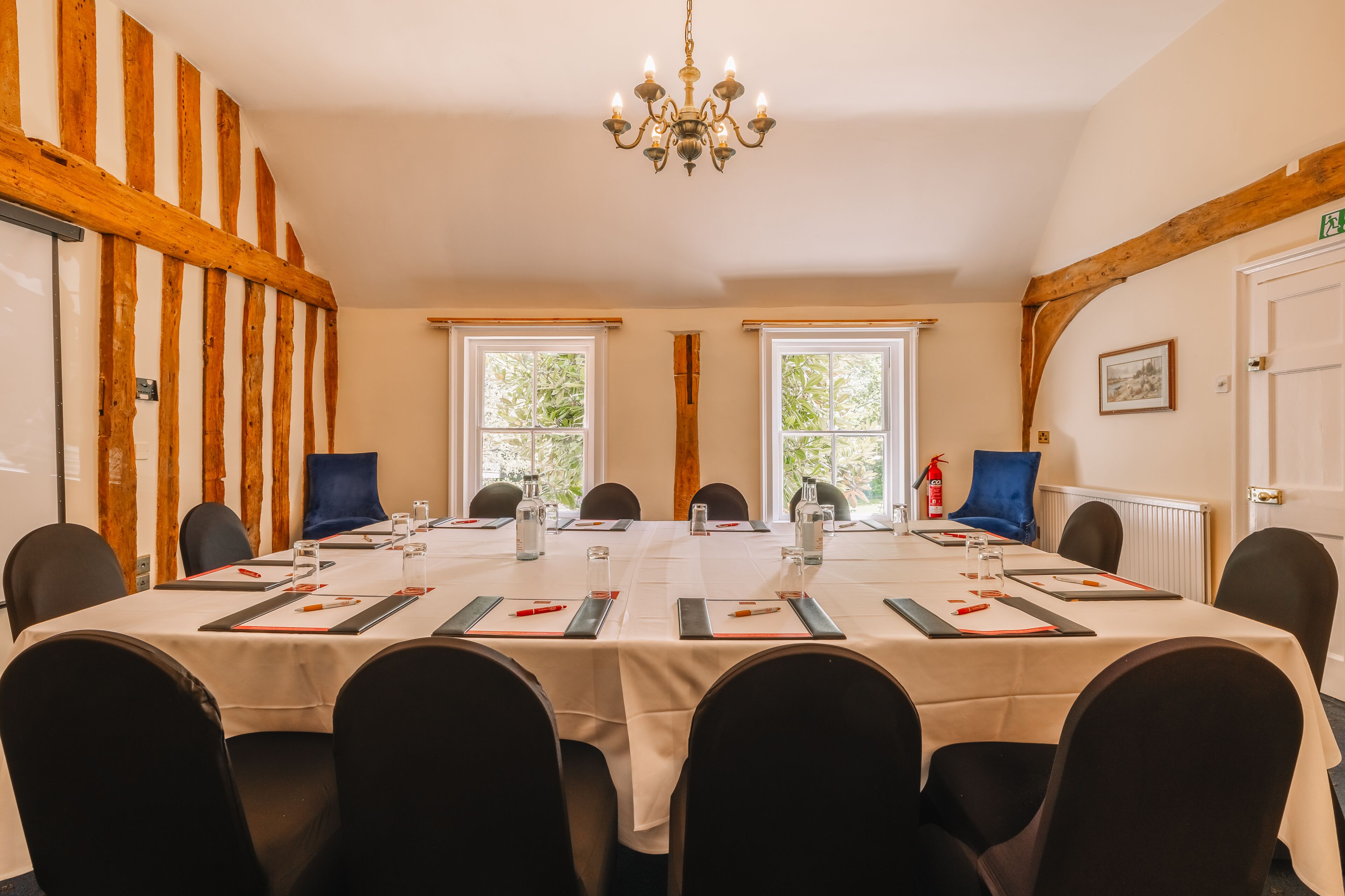 Un salón de conferencias con una larga mesa, sillas negras, manteles blancos y una araña.