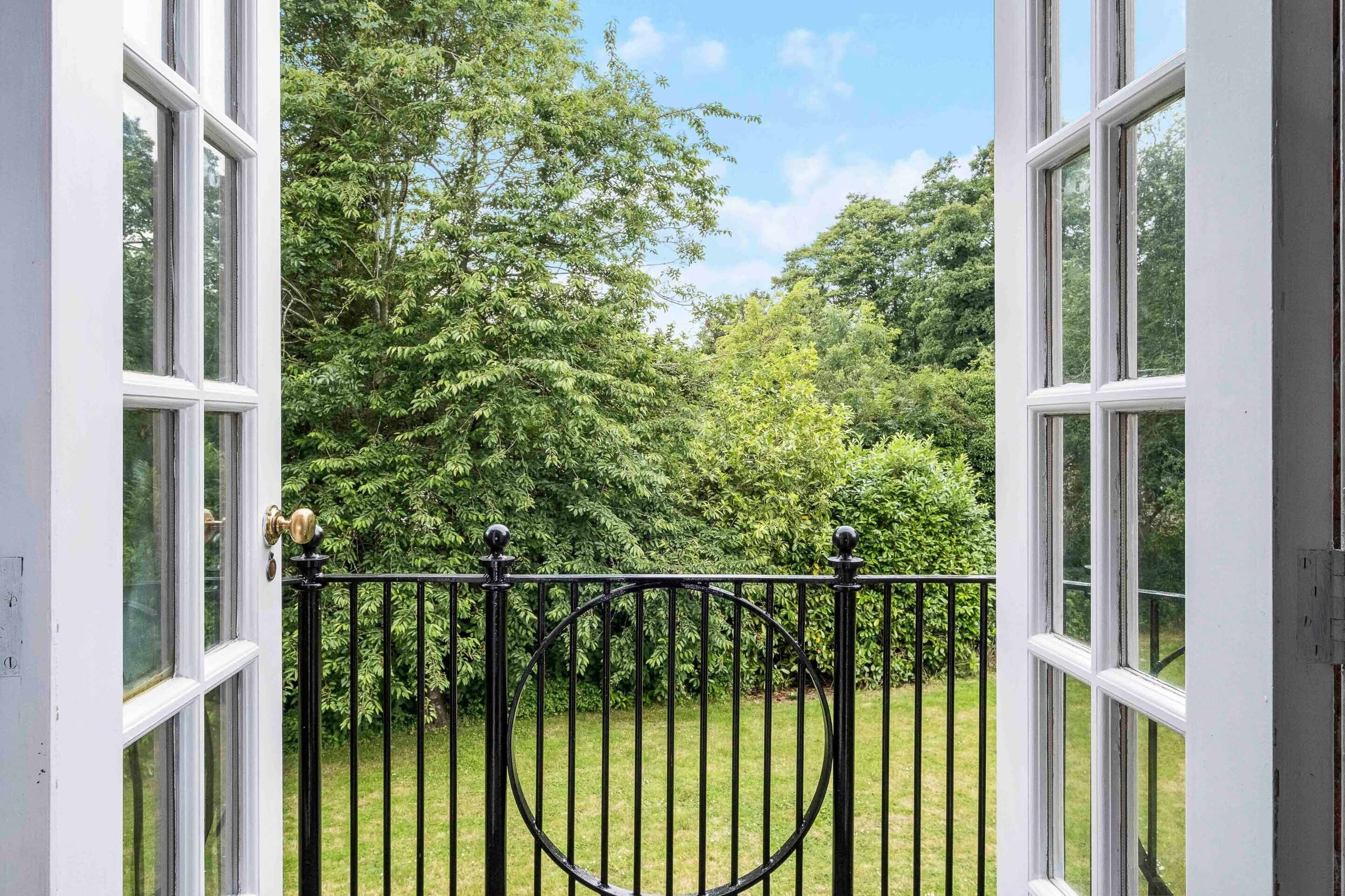 Une vue sur un jardin luxuriant, visible à travers des fenêtres ouvertes, et délimité par une clôture en métal.